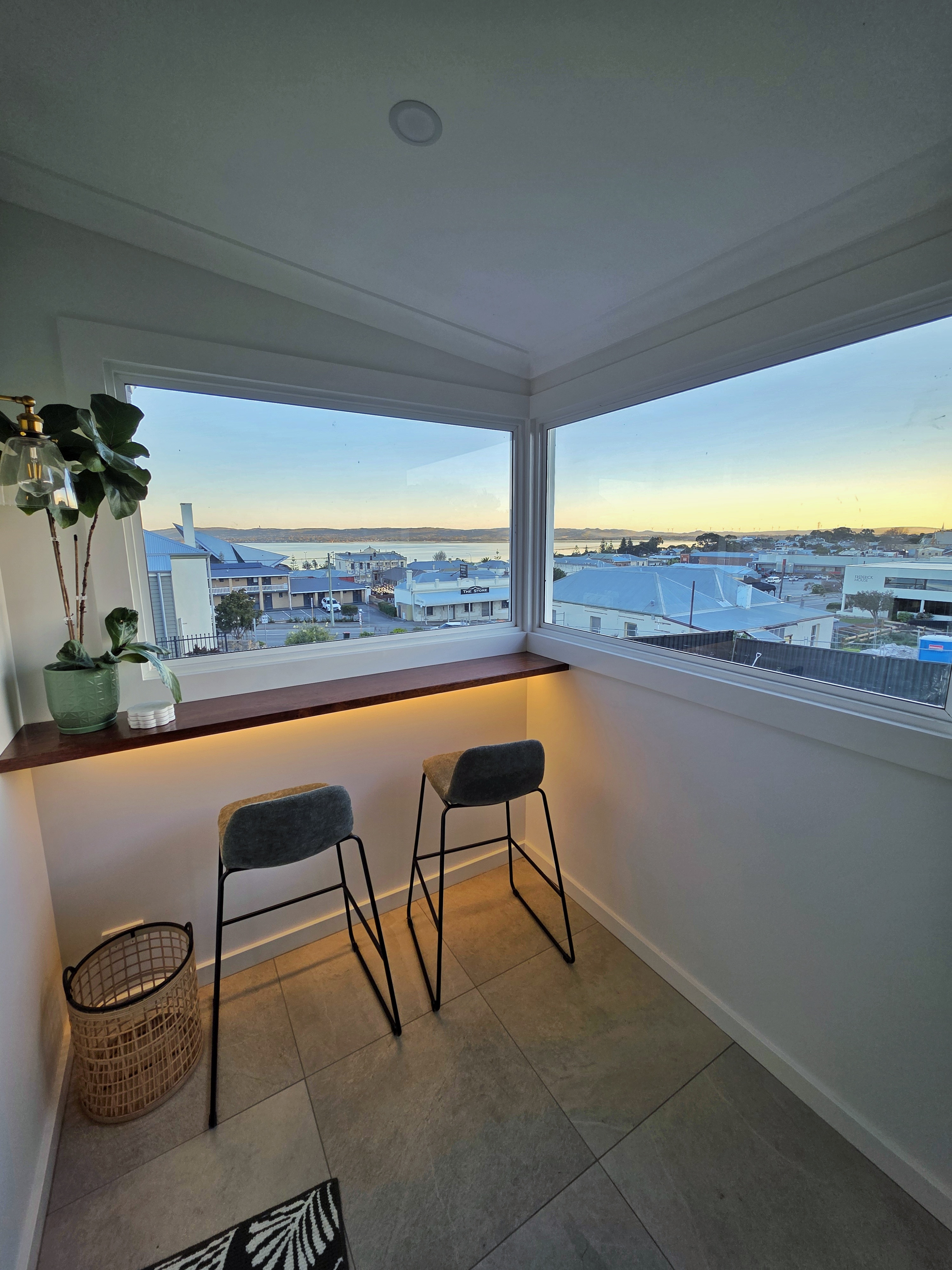 Dusk view from the sunroom window bar across Albany harbour with two stools and warm under-bench light